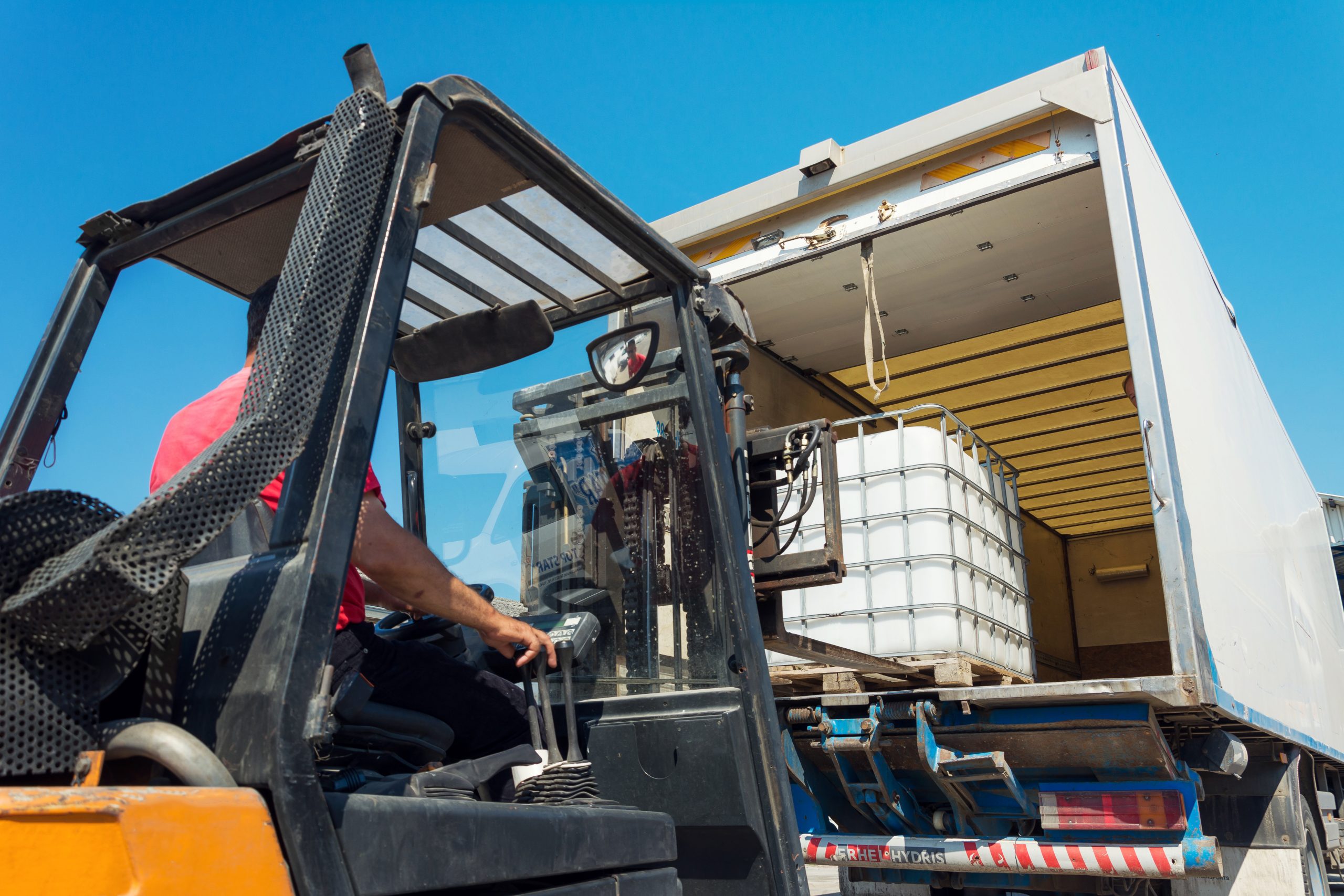 Forklift Truck Lifting White Water Tank on Pallet in Truck
